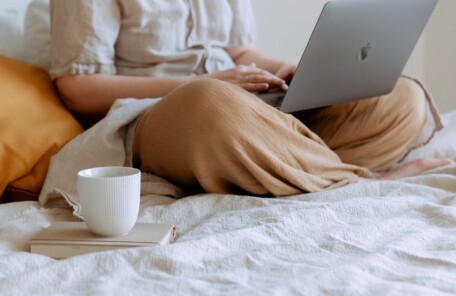 woman lounging with laptop and cup of coffee on the bed